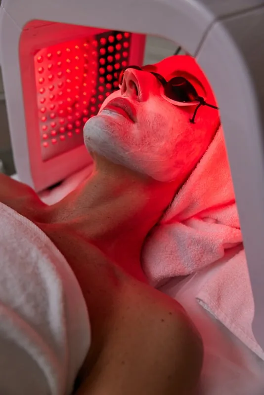 A client resting under the red light panel with eye protection